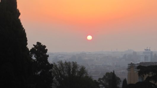 A photo of the sun rising or setting above the city scape.