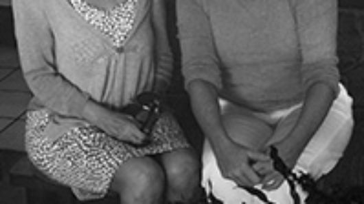 A black and white photo of two women sitting on a bench.