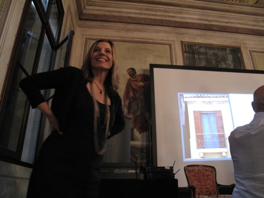 A photo of a woman giving a lecture while sitting in a renaissance era room.