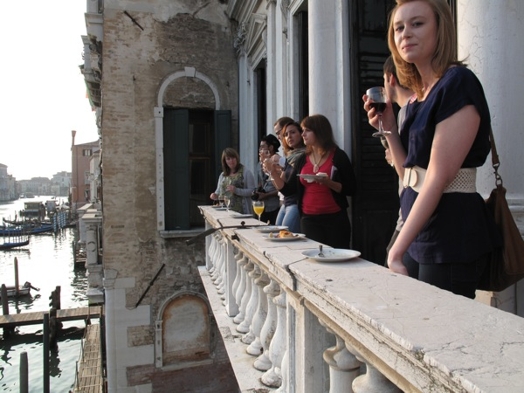 A photo of a group of people sitting at a balcony and enjoying a nice Venice view.