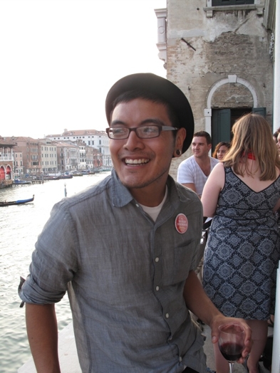 A photo of a man wearing glasses and enjoying the Venice view while drinking vine.
