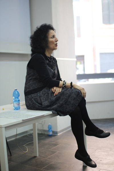 A photo of a woman sitting on a table and giving a lecture.