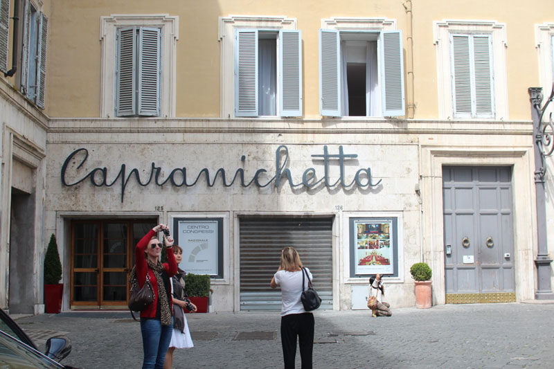 A photo of several people taking pictures while standing near a shop with the name Caprnichetta.