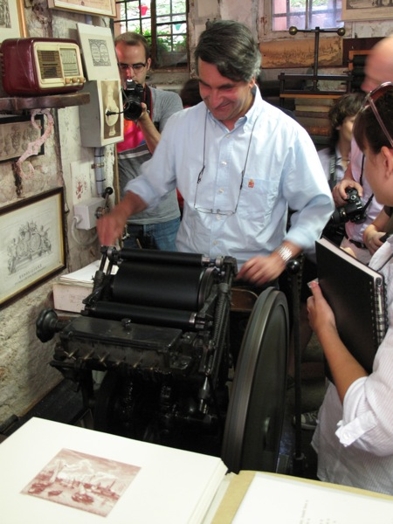 A photo of a person working an old paper press machine while other people watch.