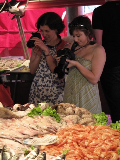 A photo of two women taking pictures at some seafood.