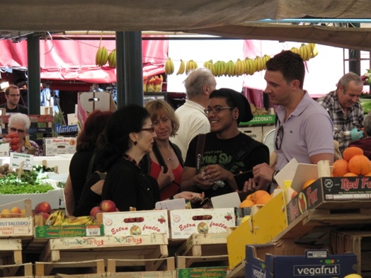 A group of people talkin while sitting in a fruit market.