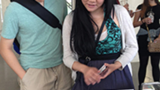 A photo of a man and a woman standing near a stand and looking at a laptop.