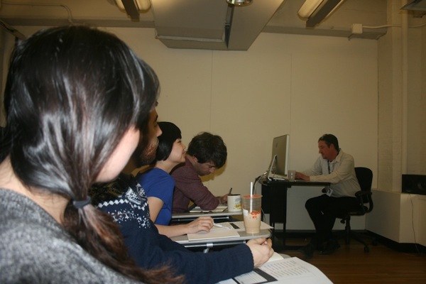 A photo of a group of students listening to a lecture given by a teacher from a computer.