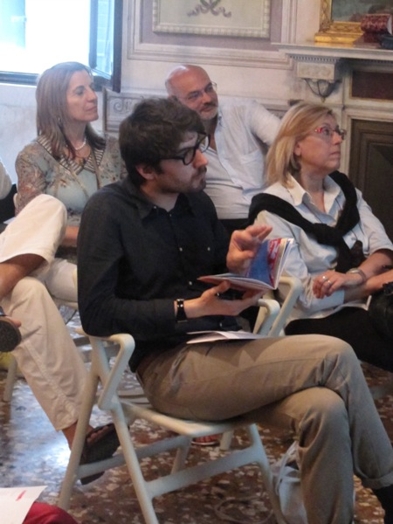 A photo of a group of people sitting on chairs, with flyers in their hands and listening to some lecture.