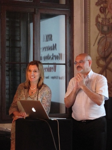 A photo of two persons giving a lecture while standing near a laptop.