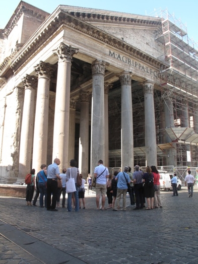 A group of people looking at an ancient stone temple in Rome.
