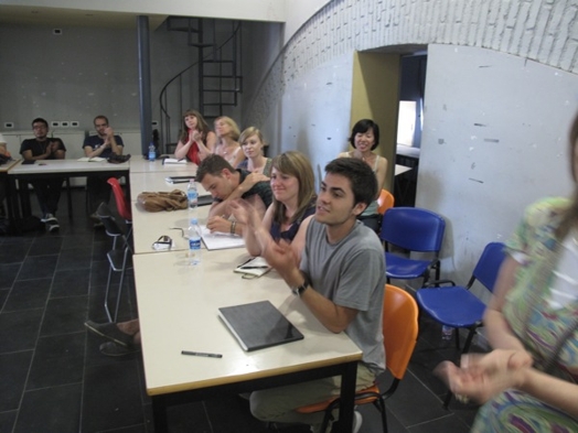 A photo of agroup of students sitting at a table and listening to a lecture.