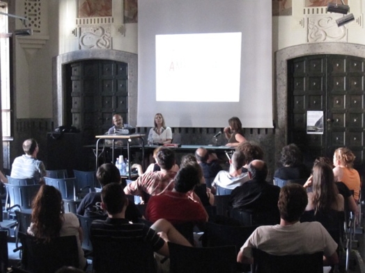 A photo of three persons giving a lecture while behind them is a screen projection.