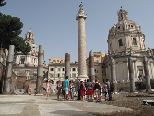 A photo of a group of people looking a stone pillar column in Rome.