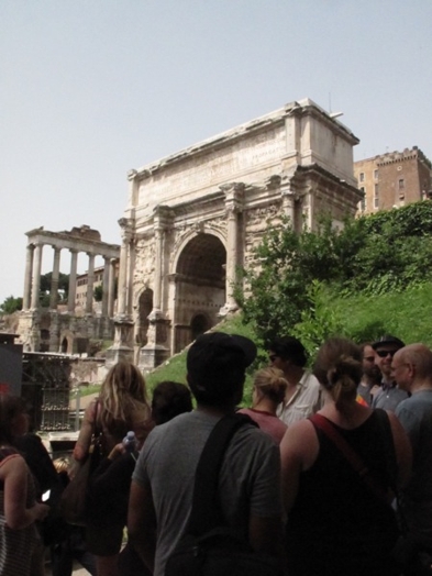 A photo of a group of people looking at an old arch building in Rome.