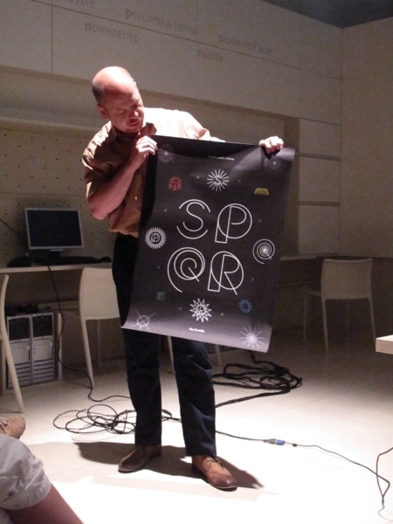 A photo of a person holding a black poster with white letters in the middle that say SPQR.