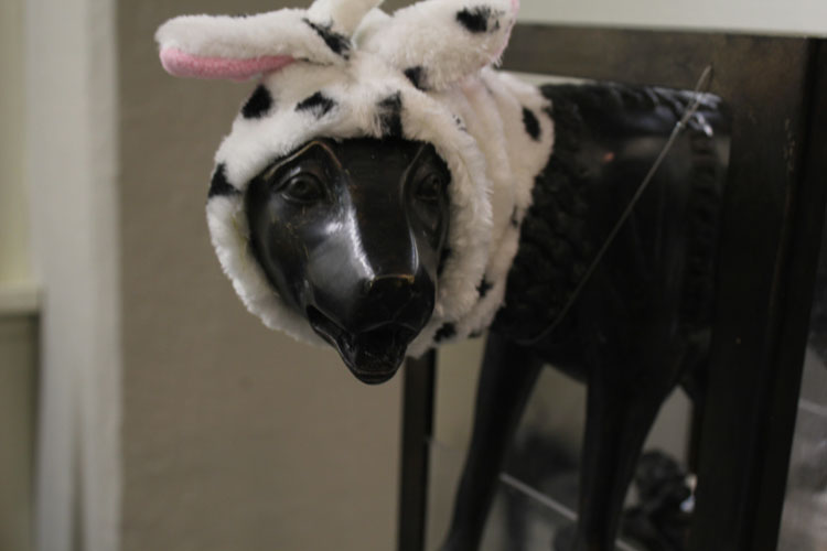 A photo of a black statue depicting a dog with a white bunny hat.