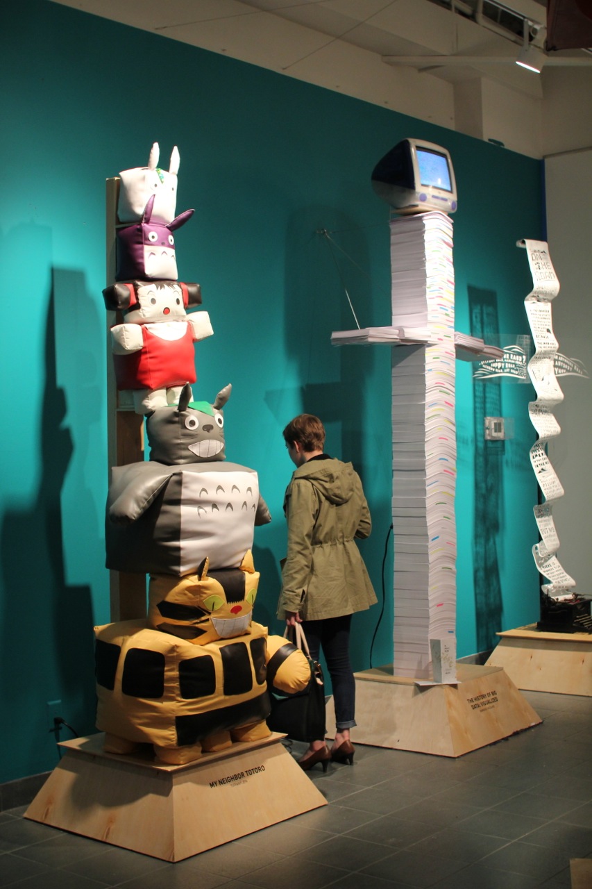 A photo of two totem looking structures, one made from cubical fluffy stuffed animals and the other made from stacked paper with a pc screen on top.