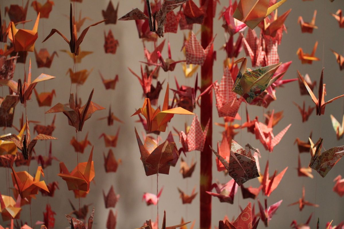 A photo of orange and red origami birds hanged with treads from the ceiling.