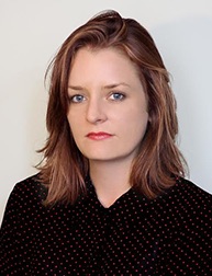 A photo of a woman wearing a black shirt and siting in front of a white wall.