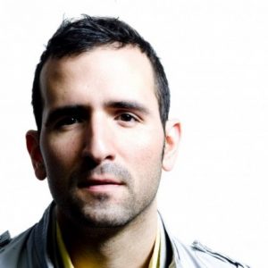 A photo of a man wearing a yellow shirt and a white coat.