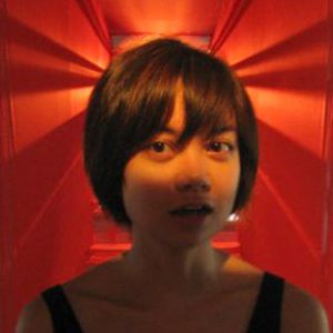 A woman in an orange red room that has half of her face illuminated.