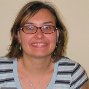 A photo of a smiling woman wearing glasses and a blue shirt with gray lines.