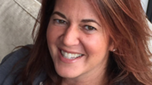 A photo of a woman sitting on a couch and smiling.