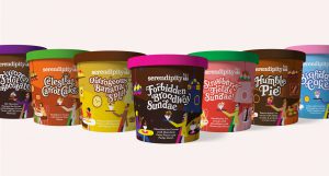A photo showing multiple ice-cream cups: one brown, purple cap with text on its side Frozen Hot Chocolate, one orange, green cap with text on its side Celestial Carrot Cake, one yellow with brown cap and text on its side Outrageous Banana Splits, one brown with pink cap and text on its side Forbidden Broadway Sundae, one red with green cap and text on its side Strawberry Fields Sundae, and one brown with brown cap and text on its side Humble Pie.