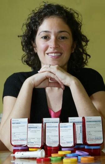 A photo of a woman, a white syringe and some rainbow colored rings used on some red pharmaceutical plastic bottles to better distinguish the pills inside.