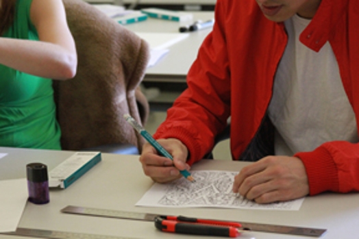 A photo of two people, each drawing a sketch on a piece of paper.
