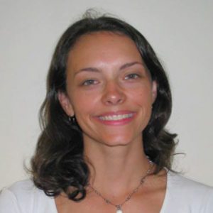 A photo of a smiling woman wearing a necklace and a white shirt.