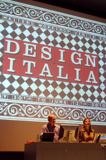 A photo of two people giving a lecture while behind them there is a projector screen with a checkered design and the text Design Italia written on some red squares.