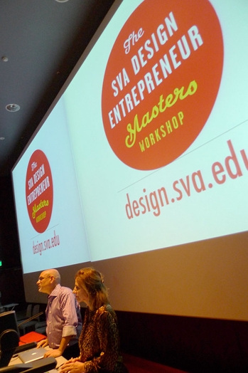 A photo of two people giving a lecture while behind them there is a projector screen with a logo and text: The SVA Design Entrepreneur Masters Workshop design.sva.edu.