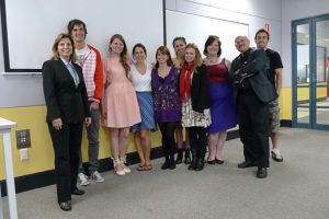 A photo of a group of people standing in a classroom with a projector screen behind them.