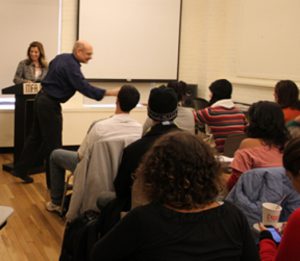 A photo showing a man giving a lecture to a group of people.