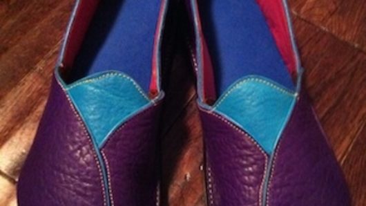 A leather pair of shoes with red, blue interior and purple green exterior with yellow threads.