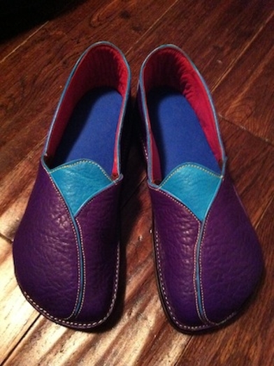 A leather pair of shoes with red, blue interior and purple green exterior with yellow threads.
