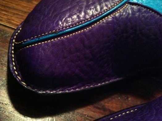A photo of a violet colored moccasin part with a cyan thread on the side.