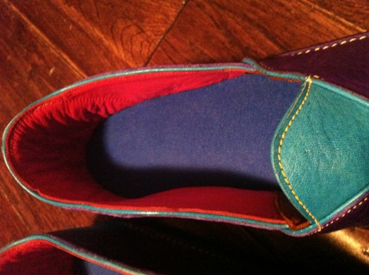A leather shoe with red, blue interior and purple green exterior with a yellow thread.