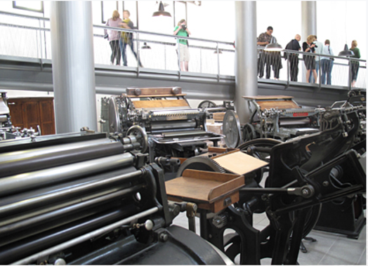 A phot of some old printing presses and some people taking pictures.