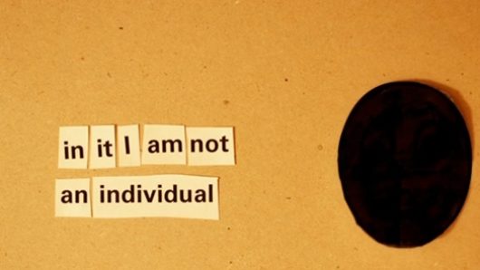 A photo of several pieces of paper, each having a word and arranged to form the text: in it I am not an individual. Near the pieces there is a round black object.