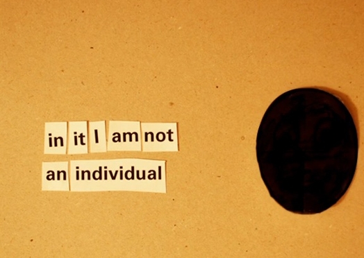 A photo of several pieces of paper, each having a word and arranged to form the text: in it I am not an individual. Near the pieces there is a round black object.