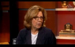 A photo of a woman wearing glasses and giving an interview.