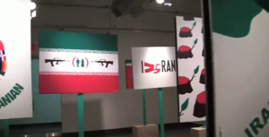 An exhibition of Iran satire, with different poles holding an Iranian flag with guns aimed on a male and female figure. Another placard has the text I Ran.