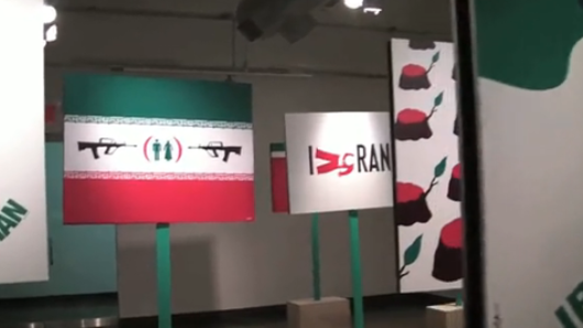 An exhibition of Iran satire, with different poles holding an Iranian flag with guns aimed on a male and female figure. Another placard has the text I Ran.