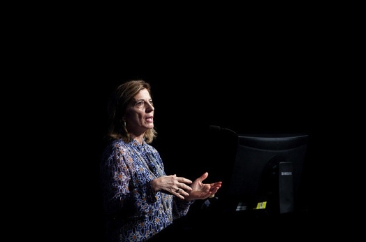 A photo of a woman with a spot light on her while giving a lecture.