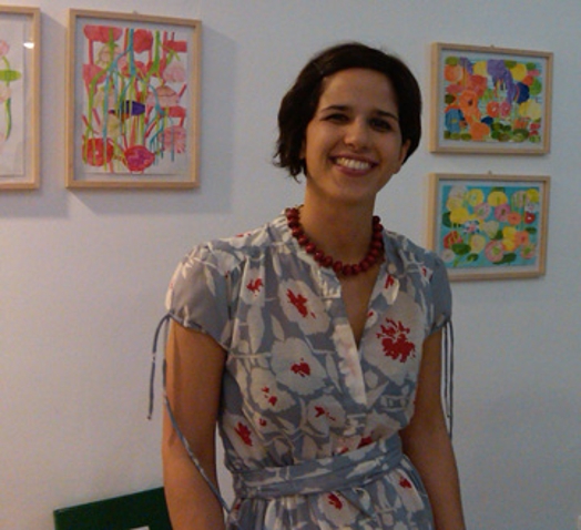 A photo of a lady wearing a flower dress and standing in front of a wall filled with multicolored flower paintings.