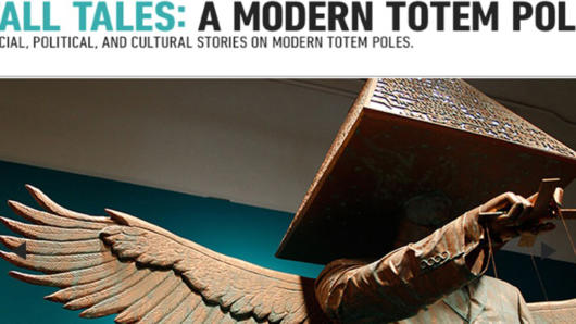 A photo of a totem pole that looks like a winged person with a pyramid on his head and pointing at something. The pyramid is covered in text. On top of the photo there is a title that says: TALL TALES: A MODERN TOTEM POLES. Social, Political and Cultural Stories on Modern Totem Poles.