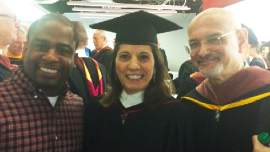 A photo of three people in a hall, one of them just graduated.